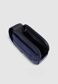Marineblauwe tas met een rechthoekige vorm, gemaakt van textuurrijke en gladde materialen. Heeft meerdere vakken en een ritssluiting.