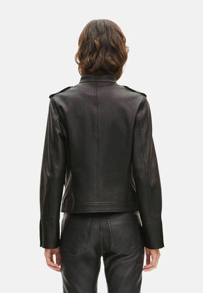 Veste en cuir noir avec une coupe ajustée, des épaulettes et des manches structurées, présentant une texture lisse et des coutures nettes.