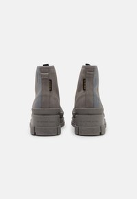 Botines de ante gris con un diseño de caña alta, que presentan acentos en negro y amarillo, suelas de goma gruesas y un logotipo grabado en la parte trasera.