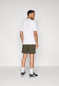 Bijela majica s kratkim rukavima, maslinaste kratke hlače, crne sportske cipele, bijele čarape. Jednostavan dizajn bez vidljivih uzoraka ili naglasaka.