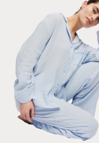 Ljusblå, knäppbar pyjamasset i texturerad bomull. Har en bröstficka och långa ärmar med uppvikt kant. Löst sittande design.