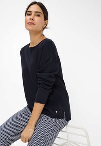 Navy lange mouw top met een relaxed fit en ronde halslijn, gecombineerd met gestreepte navy en witte broek met een geometrisch ontwerp.