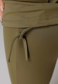 Olijfgroene sportkleding tailleband met een trekkoord, gemaakt van glad, rekbaar materiaal; zichtbare stiksels langs de rand.