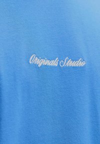 Sinine puuvillane T-särk, millel on valgest kirjaga "Originals Studio" brodeeritud. Sile tekstuur klassikalise ümmarguse kaeluse disainiga.