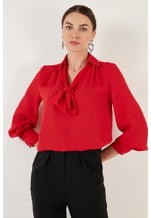 Red blouse with a tie bow at the collar, pleated shoulders, and long sleeves featuring buttoned cuffs. Made of lightweight fabric.