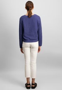 Fialový rebrovaný pletený sveter s dlhými rukávmi, okrúhlym výstrihom a voľným strihom, skombinovaný s bielymi skrátenými džínsami a čiernymi sandálmi.