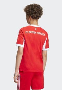 Rød fotballtrøye med hvite detaljer, som har "FC Bayern M�ünchen" på ryggen. Korte ermer, rund hals, laget av pustende stoff.