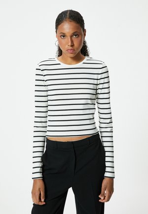 Witte langemouwen top met zwarte horizontale strepen, ronde halslijn en een cropped ontwerp. Draag het met zwarte high-waisted broek.
