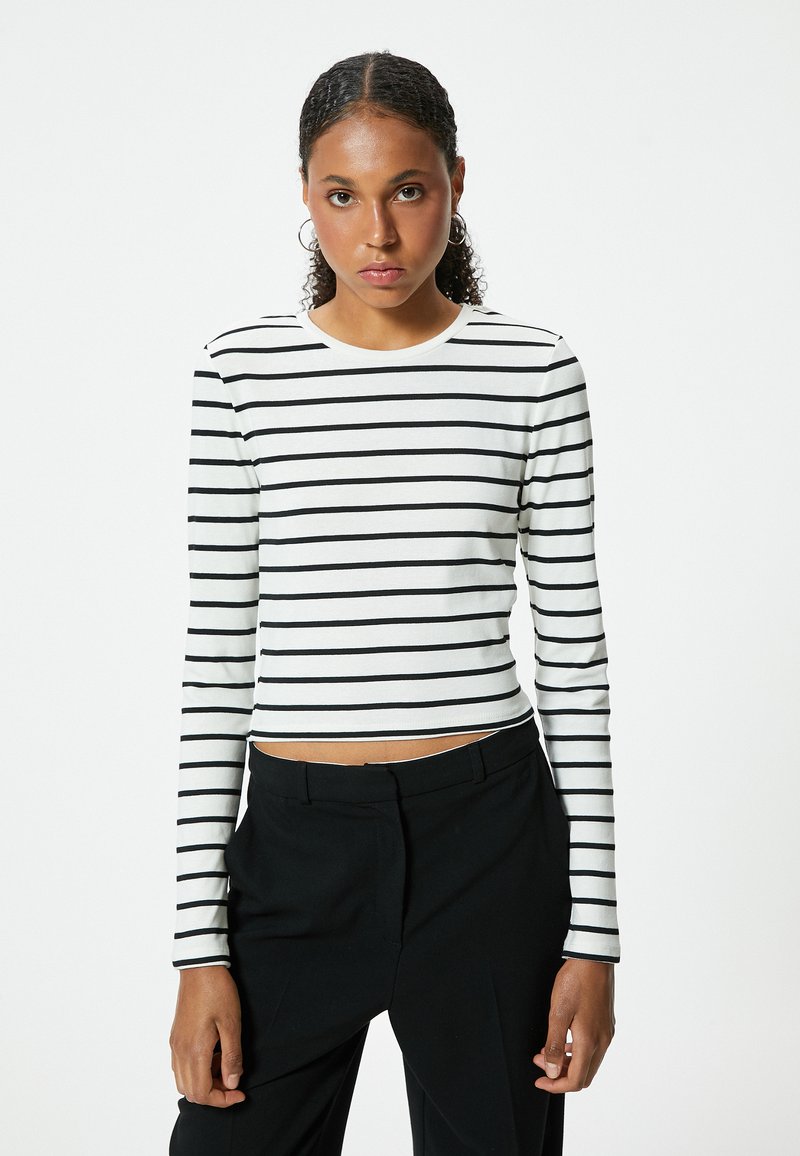 Witte langemouwen top met zwarte horizontale strepen, ronde halslijn en een cropped ontwerp. Draag het met zwarte high-waisted broek.