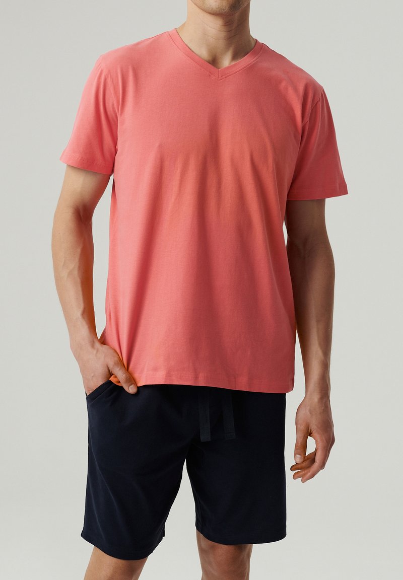 T-shirt z krótkim rękawem w kolorze koralowym, z dekoltem w serek, o luźnym kroju i gładkiej fakturze, zestawiony z granatowymi szortami z kieszeniami.