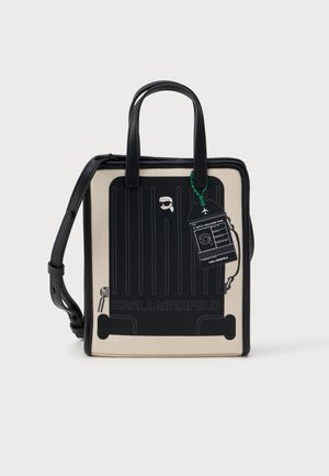 Vierkante beige en zwarte handtas met zwarte handvatten, kofferafbeelding en aangehecht bagagelabel met een gestileerd gezicht met zonnebril.