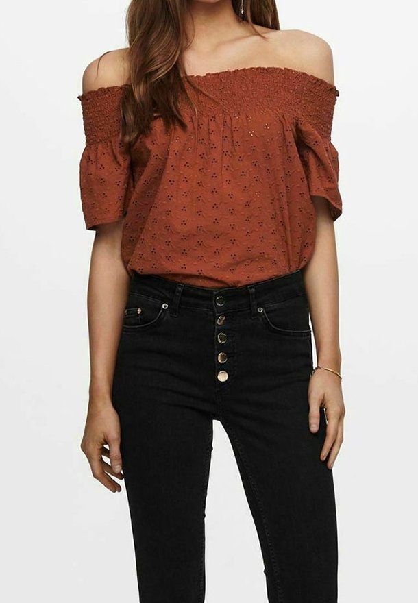 Rustfarvet off-the-shoulder bluse med mønstret tekstur, korte puffærmer, parret med højtaljede sorte jeans med guldknapper.