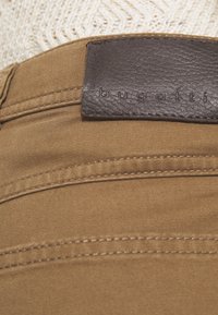 Bruine stoffen broek met een gladde textuur, voorzien van een donkerbruine leren label met het reliëf "bugatti" en contrasterende stikseldetails.