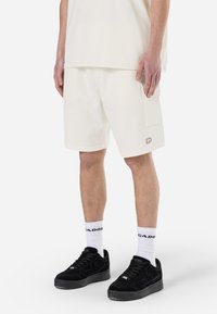 Hvide bomulds shorts med en afslappet pasform, sidelommer og et lille logo påsyet. Kombineret med sorte sneakers og hvide ankelstrømper.