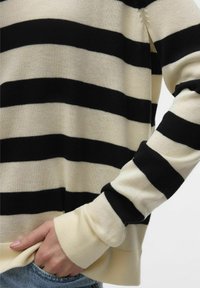 Maglione a righe nero e crema con una vestibilità rilassata, caratterizzato da un collo e polsini a costine. La trama sembra morbida e lavorata a maglia.