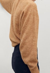 Maglione marrone chiaro con una vestibilità rilassata, polsini a coste e dettagli delle spalle senza cuciture, abbinato a jeans scuri a vita alta.