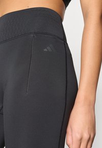 Leggings de sport noirs avec une ceinture texturée, portant un petit logo noir et des détails de couture visibles sur les poches latérales.