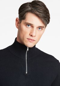 Schwarzer Reißverschluss-Pullover mit hohem Kragen, ausgestattet mit feinem Rippenmuster und einem silbernen Zipper, entworfen für eine taillierte Passform.