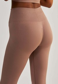 Legginsy o wysokim stanie, dopasowane do sylwetki, wykonane z miękkiego, matowego materiału w kolorze przykurzonego różu, z delikatną, ukośną teksturą prążkową i elastycznym materiałem.