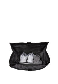 Sac de sport noir avec un extérieur lisse. Contient des baskets blanches, une serviette grise roulée et un compartiment zippé en bas.