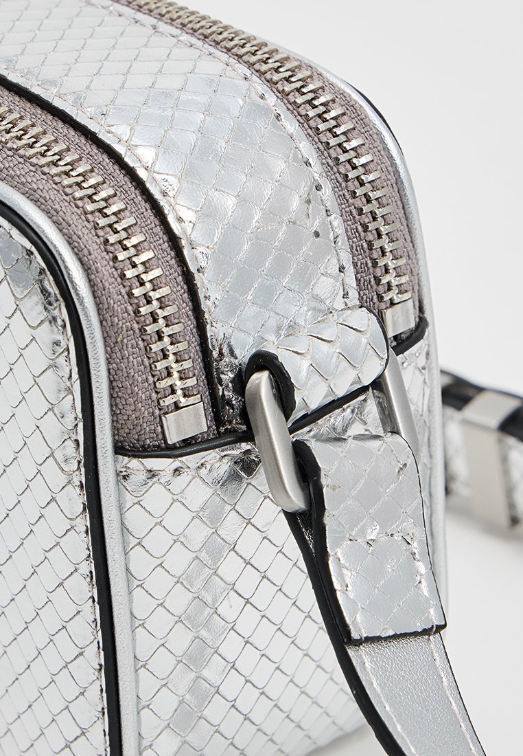 Srebrna metaliczna torebka z teksturowanym wzorem wężowej skóry, z podwójnymi zamkami błyskawicznymi i szarym materiałowym akcentem wzdłuż góry.