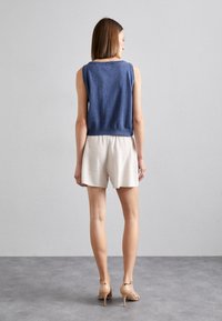 Blå ermeløs topp med en avslappet passform, kombinert med lysebeige shorts. Toppen har en jevn tekstur og ensfarget design, mens shortsen er lett teksturert.