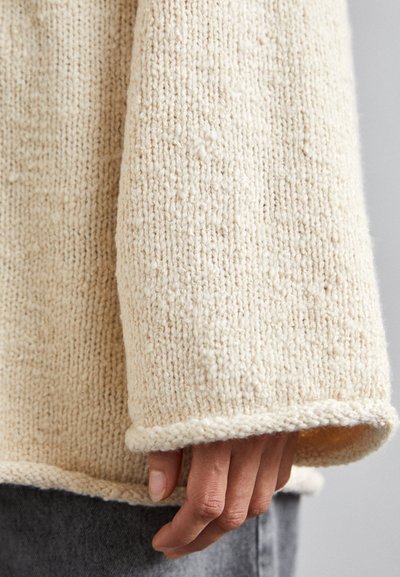 Κρεμ μπλε πλεκτό πουλόβερ με υφή, φαρδιά μανίκια και χαλαρή εφαρμογή. Το ύφασμα φαίνεται μαλακό με ορατές λεπτομέρειες ραφής.