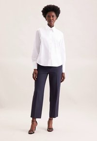 Witte overhemd met knopen en een klassieke kraag, gecombineerd met marineblauwe broek met rechte pijpen. De stof oogt glad, met minimalistische ontwerpdetails.