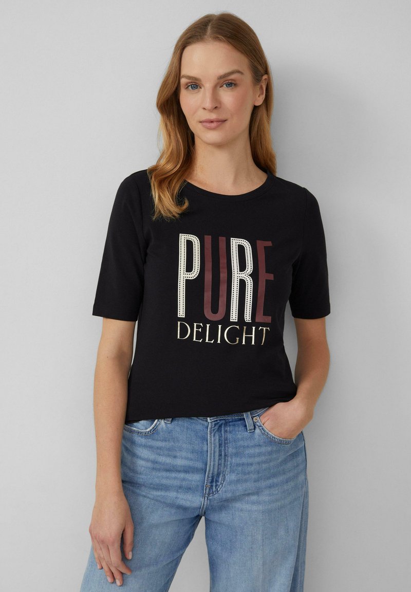 T-shirt en coton noir à manches courtes avec le texte "PURE DELIGHT" en blanc et bordeaux, porté avec un jean bleu clair.