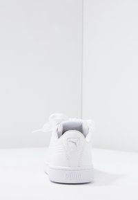 Scarpe da ginnastica bianche con una tomaia in pelle liscia, forma arrotondata, suola piatta e un grande fiocco sulla parte anteriore; presentano un logo sul tallone.