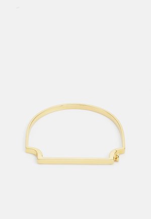 Goldfarbener Armreif mit minimalistischen Design, der eine glatte, geschwungene Form und einen rechteckigen Akzent auf einer Seite aufweist.