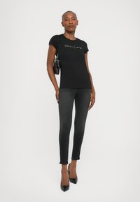 Zwarte aansluitende T-shirt met korte mouwen, met een gouden geborduurde merknaam. Gecombineerd met donkere skinny jeans en zwarte hoge hakken.