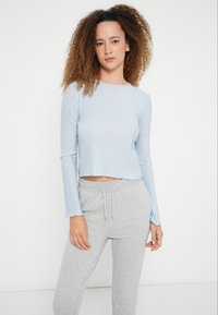 Lichtblauw geribbeld crop top met lange mouwen en een golvende zoom, gecombineerd met grijze joggingbroek met trekkoord. Gladde textuur, casual pasvorm.