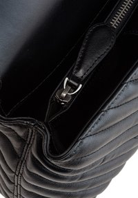 Zwarte leren handtas met een gequilt ontwerp, voorzien van een ritssluiting en zilveren hardware. Gladde textuur en zachte, ronde randen.