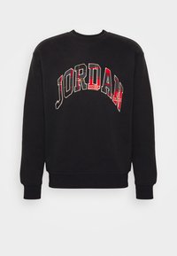 Svart hoodie med långa ärmar som har "JORDAN" i stora, bågformade bokstäver med ett rött och rutigt mönster över bröstet.