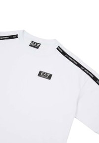 T-shirt bianca in cotone, con una patch logo nera e accenti neri sulle maniche. Collo rotondo classico; maniche corte.