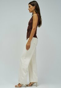 Un débardeur marron à côtes associé à un pantalon large blanc taille haute et des talons à lanières, affichant une silhouette épurée.