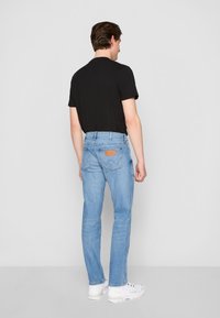 Heledad sinine denim teksad sirge lõikega, tagaküljel on detail, millel on kontrastne tikand, koos musta t-särgi ja valgete tossudega.