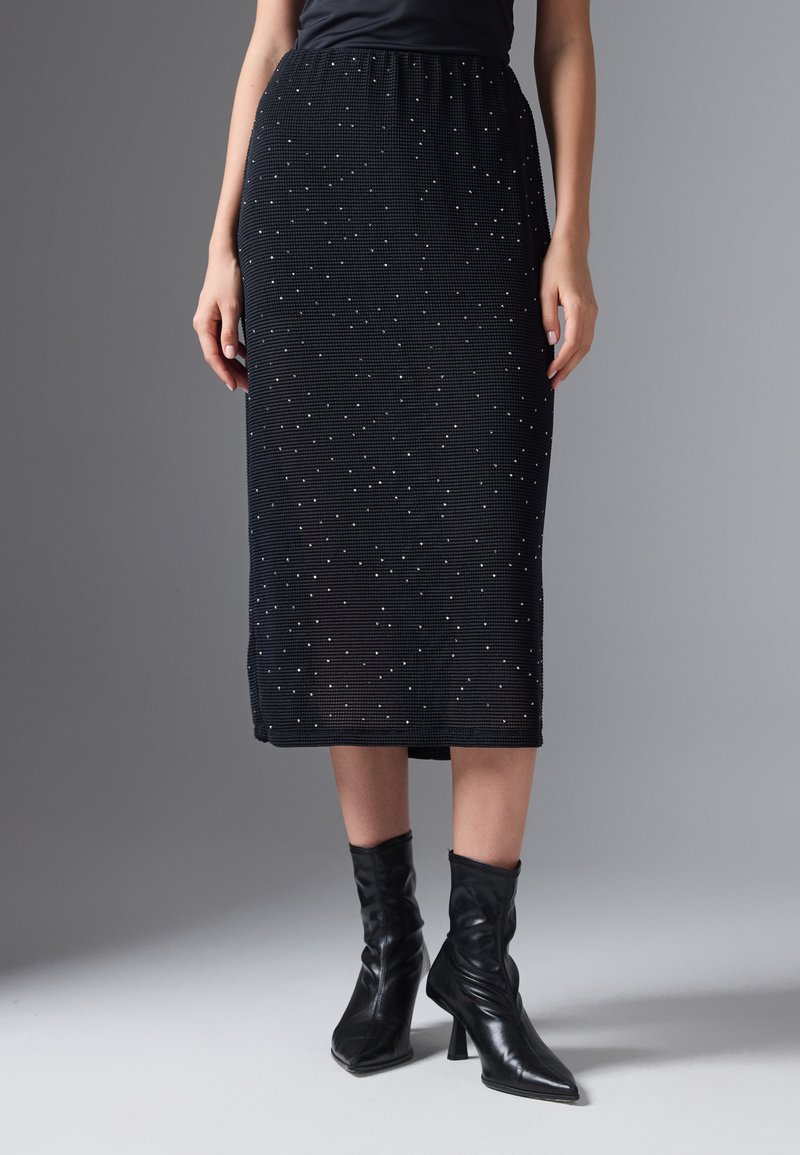 Schwarzer gerippter Rock in knielanger Länge mit silbernen Punktverzierungen, ausgestattet mit einem gerafften Taillenbund und kombiniert mit eng anliegenden schwarzen Ankle Boots.