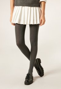 Šedé texturované punčocháče s mírným leskem, nošené s plisovanou bílou sukni a černými mokasíny s masivní podrážkou.