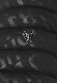 Sort pufferjakke stof med en subtil mønstret tekstur, udstyret med et trekantet logo i sort, prydet med glitrende detaljer.