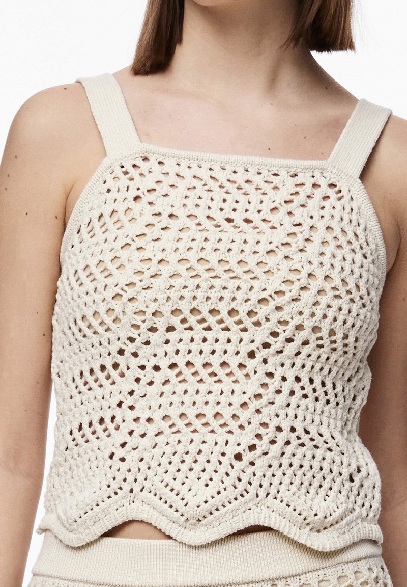 Top sin mangas de ganchillo en color crema, con un patrón de diamantes, tirantes anchos y un dobladillo en forma de concha. Fabricado con hilo texturizado.