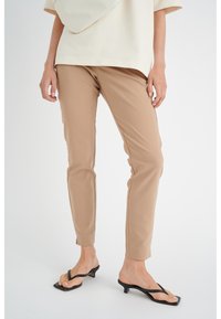 Beige skræddersyede bukser i blød stof, tapered ben design og mellemhøj talje, parret med sorte toe sandaler med en lille hæl.