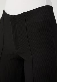 Schwarze gerippte Hose mit glatter Textur, ausgestattet mit einem hohen Bund und seitlichen Taschen. Enganliegendes Design an den Hüften.