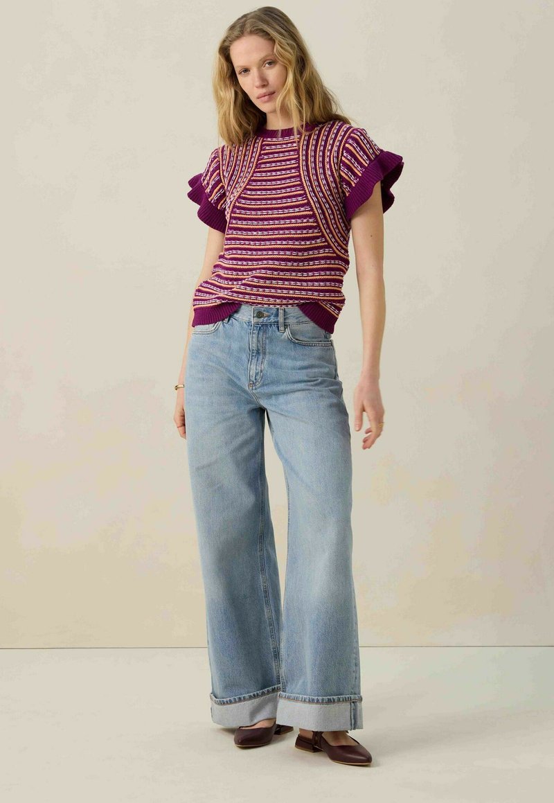Haut en tricot violet avec un motif rayé et des manches ruffle courtes, associé à un jean large bleu clair et des chaussures plates brunes.