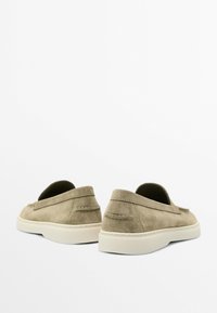 Suede slip-on shoes in olive green with a textured finish, white rubber soles, and discreet stitching detail at the heel.