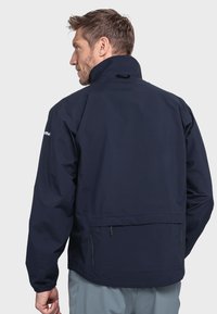 Marineblaue wasserdichte Jacke mit hohem Kragen, elastischen Bündchen und Seitentaschen. Sanfte Textur und minimales Design mit dezenten Hardware-Details.