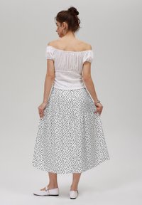 White off-the-shoulder top with textured fabric and puff sleeves, paired with a white skirt featuring black polka dots and tiered design. White shoes.