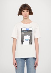 Weißes Baumwoll-T-Shirt mit einem grafischen Druck, der ein Gesicht, blaue Lippen und ein blaues Herz zeigt. Das Design enthält kräftige schwarze Konturen und Text.