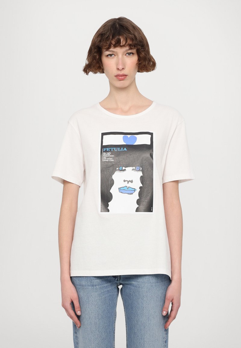Hvit bomulls T-skjorte med grafisk trykk av et ansikt, blå lepper og et blått hjerte. Designet inkluderer fete sorte konturer og tekst.